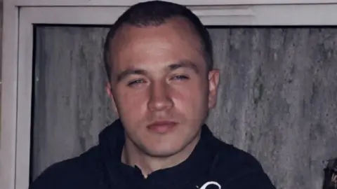 A man with short dark hair is seen looking at the camera