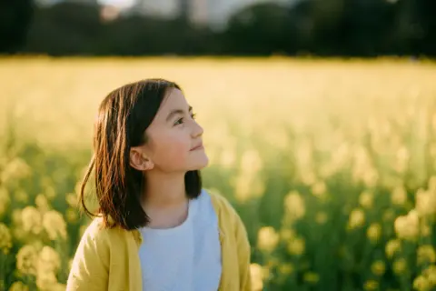 A young girl stands in a field of yellow blossoms