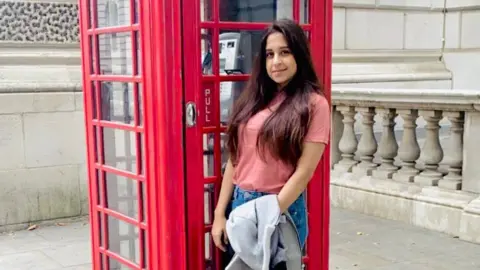 Raheema Ahmed Raheema standing in front of a telephone box 