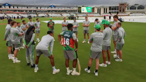 Leicestershire players in a huddle with covers on the pitch behind