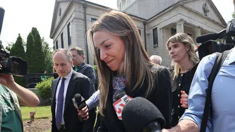 Getty Images/Boston Globe Karen Read smiling outside court being asked questions by reporters.
