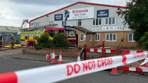 Richard Knights/BBC The outside of Britannia Alan Cook, a storage and removals warehouse located on an industrial estate. A red fire engine is parked outside the front of the building and a DO NOT CROSS cordon has been put in place.