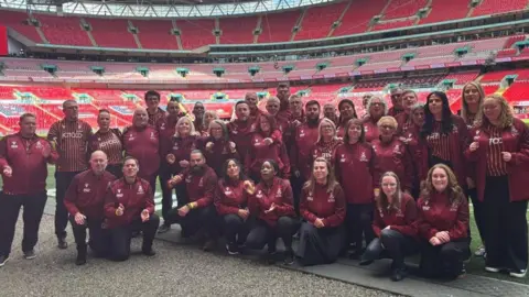 Bantam of the Opera A mixed gender and aged group of people wearing Bradford City FC branded outfits, pose together in a football stadium. 