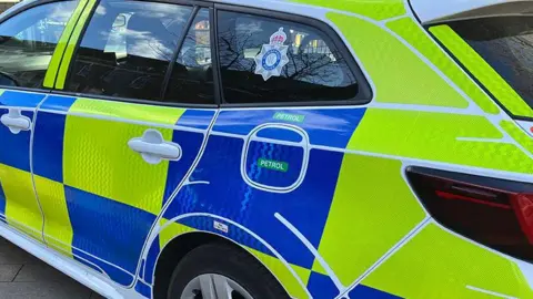 BBC A police car is parked up on a road. I has blue and yellow police markings and a Humberside Police logo in the rear passenger window.