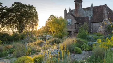 National Trust An old English brick house surrounded by a garden of green, Mediterranean plants.