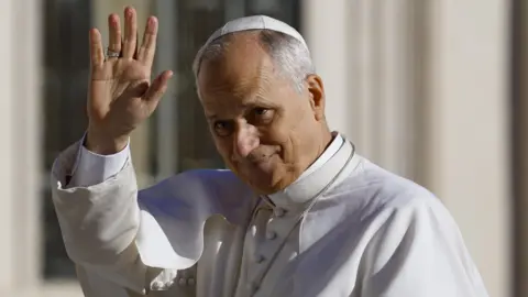 EPA Pope Leo XIV wearing white papal attire. He is raising his hand as if he is waving.