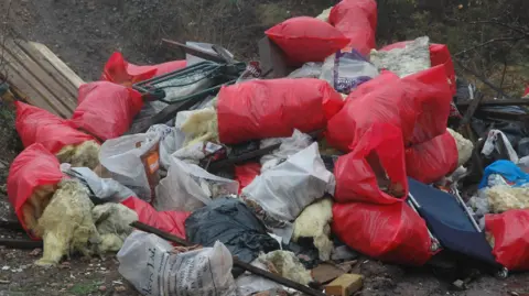 CLA A pile of red bin bags and insulation on the ground.