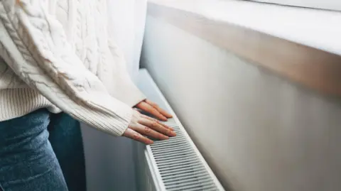A person wearing a white jumper is holding their hands over a radiator.