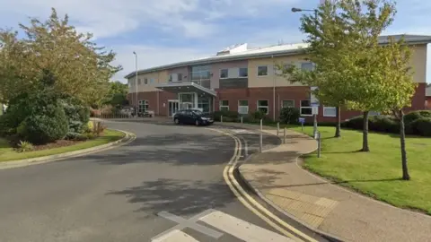 Curved road in front of brown and yellow hospital building. 