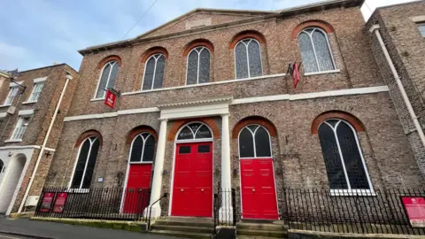 Supplied An image of The Wesley Centre. It is a traditional Methodist church style building with bright red doors 