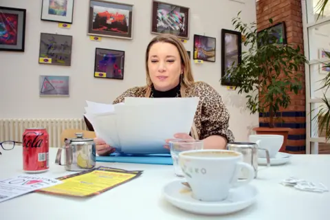 Chloe Smith looks over writing projects from her group as she drinks a cup of tea