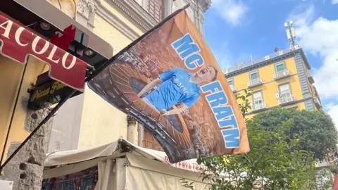 Flag bearing an image of Scott McTominay and the words McFratm hangs out of a building in Naples