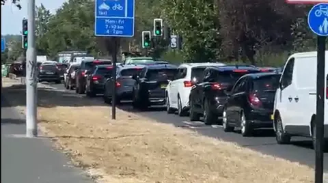 SHAM ASHRAF Daytime traffic jam on a road, showing a long queue of cars and a white van stationary near traffic lights, with blue road signs for bus and cycle lanes visible in the foreground.