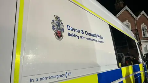 The photo shows a close-up of the side of a Devon and Cornwall police van with the words 'building safer communities together' printed on the side.