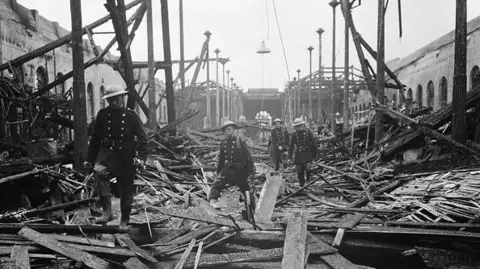 Getty Images People in uniform are picking their way through debris at Market Hall after an air raid during the blitz in Birmingham around 1940. There is rubble all around them and half-standing structures in the black and white archive image.