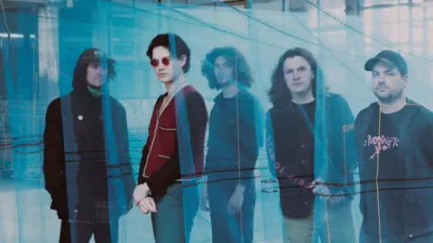 Rothco Five young men stand behind sheets of see-through blue fabric.