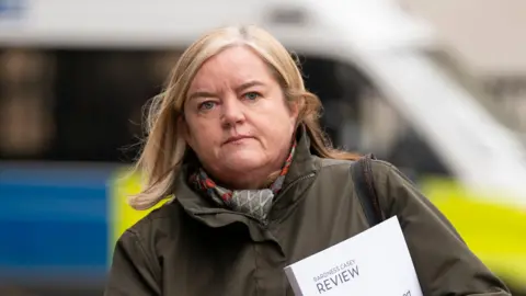 PA Media Image from 2023 of Baroness Louise Casey holding a copy of her previous review into police culture as she walks to a conference. She is wearing a dark coat and scarf