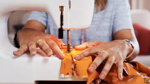 Getty Images 一名女子使用缝纫机修补一件彩色衣物的图片