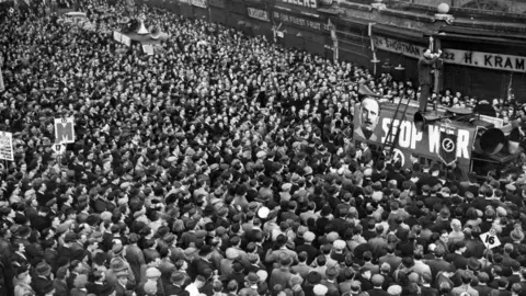 Getty Images A huge crowd of people listening to someone speaking on a bus. 
