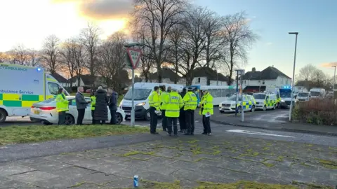 a group of police officers stand in a circle in front of a row of emergency vehicles