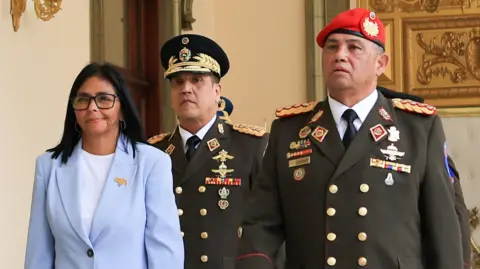 Venezuela's acting President Delcy Rodríguez walks with Gen Gustavo González López in Caracas, Venezuela, on 19 March. She is wearing a light blue jacket and white shirt, while Lopez is wearing military uniform, including a red beret.