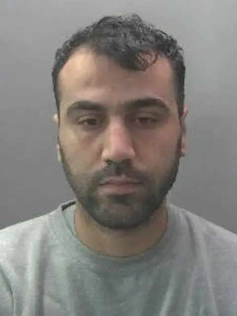 Cambridgeshire Police A police photograph of a dark-haired man with a dark beard wearing a round-necked grey T-shirt.