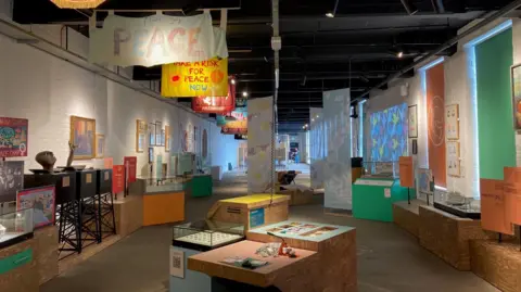 Peace banners hanging from the ceiling of a long room which also has exhibits and display cases along both walls.  