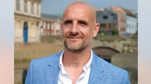 Austen Moore Councillor Austen Moore wears a light blue linen suit and white shirt.