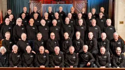 Bath Male Choir A group photo of a male choir. The members are wearing black shirts. They are sitting in rows and smiling at the camera.