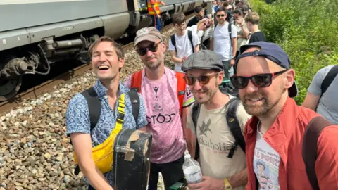 Stornoway Four members of the band Stornoway stand in a group of people outside the broken-down train