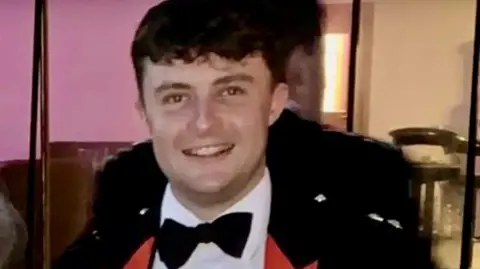 Captain Philip Gilbert Muldowney smiles as he looks into the camera, with short dark hair, wearing a dress suit and bow tie.
