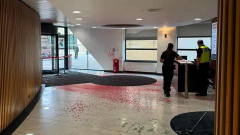 Supplied The inside of the office building a woman stands with a police officer at the reception desk. Red paint has been sprayed across the marble floor and up a wall. A window on the door has been smashed and pieces of glass litter the floor.