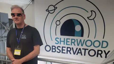 Dr Steve Wallace in shades by a sign for the observatory