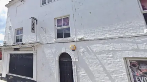 Zinc nightclub in Trowbridge - a white-painted brick building with black-out windows, posters and 'Zinc' signs, on the side of a street.