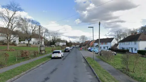 A residential street lined with white houses and grass. 