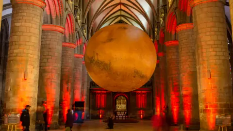 Ella Foster/Exeter Cathedral A large red coloured orb suspended between stone arches