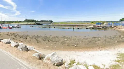 Harbour with jetty stretch out into the water.  Boats are seen moored up to the left, a bridge is in the distance over the water to the right.