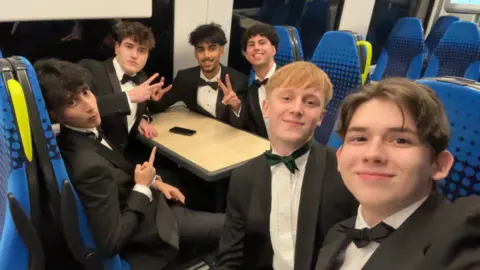 Oles Kuzomko Six men sat on a train wearing black suits and black bowties. 
