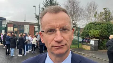 A close-up of Kingston. He has short gray hair, wears glasses and a navy blue suit.