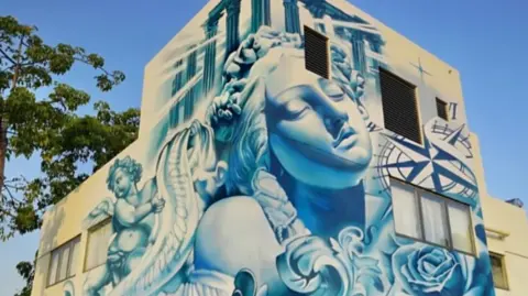 Southend-on-Sea City Council A blue and white mural is on the side of a building. The art work is of a Greek goddess which has a rose and a compass near them.