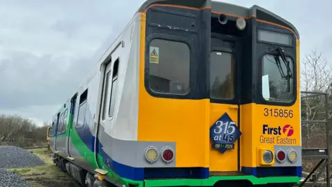 ACMU Society A closer look at the front end of the partially restored 315 train. On its front, the First Great Eastern logo can be seen as well as the train's number, 315856. Red and white lights are either side of the front of the train. 
