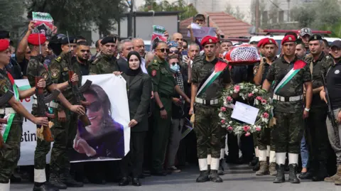 EPA Palestinian honour guards hold aloft the wrapped body of Ms Eygi on a stretcher amid a crowded turnout for her funeral procession in Nablus on 10/9/2024.