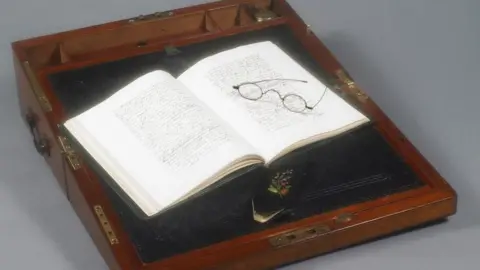 British Library Jane Austen's wooden writing box open with an open book of hand-written text and a pair of spectacles resting on the right hand page