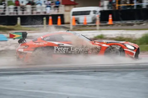 Bourne HPP A red and black Mercedes driving on a wet race track with muddy water spraying out from underneath the car.
