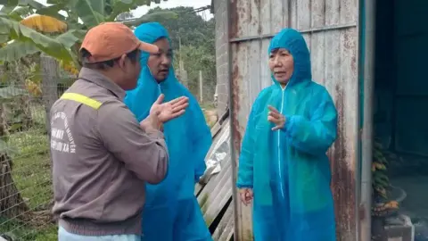 FAO officials in blue overalls talk to a Vietnamese farmer in front of a barn