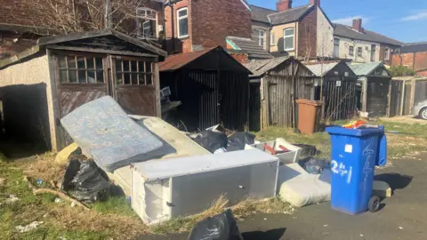 Photograph of fly-tipping next to garages behind houses in the Guide Bridge area of Ashton under Lyne.