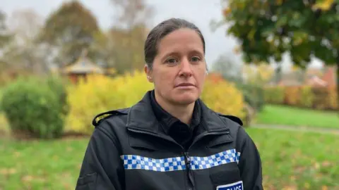 PC Coates is standing in a park and looking straight-faced. She is wearing a uniform.