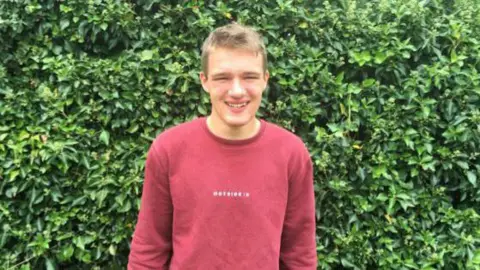 Kyle Bradshaw in red jumper standing in front of a bush