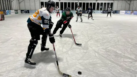 BBC Two ice hockey players vying for the puck in the rink. There are several players in the background. 