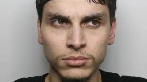 A police mug shot of Parampreet Singh, who has a wispy beard, black hair and is looking off to the side